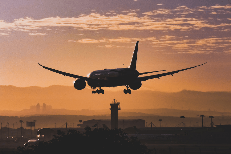 A pax aircraft flying low over an airport against an orange sky